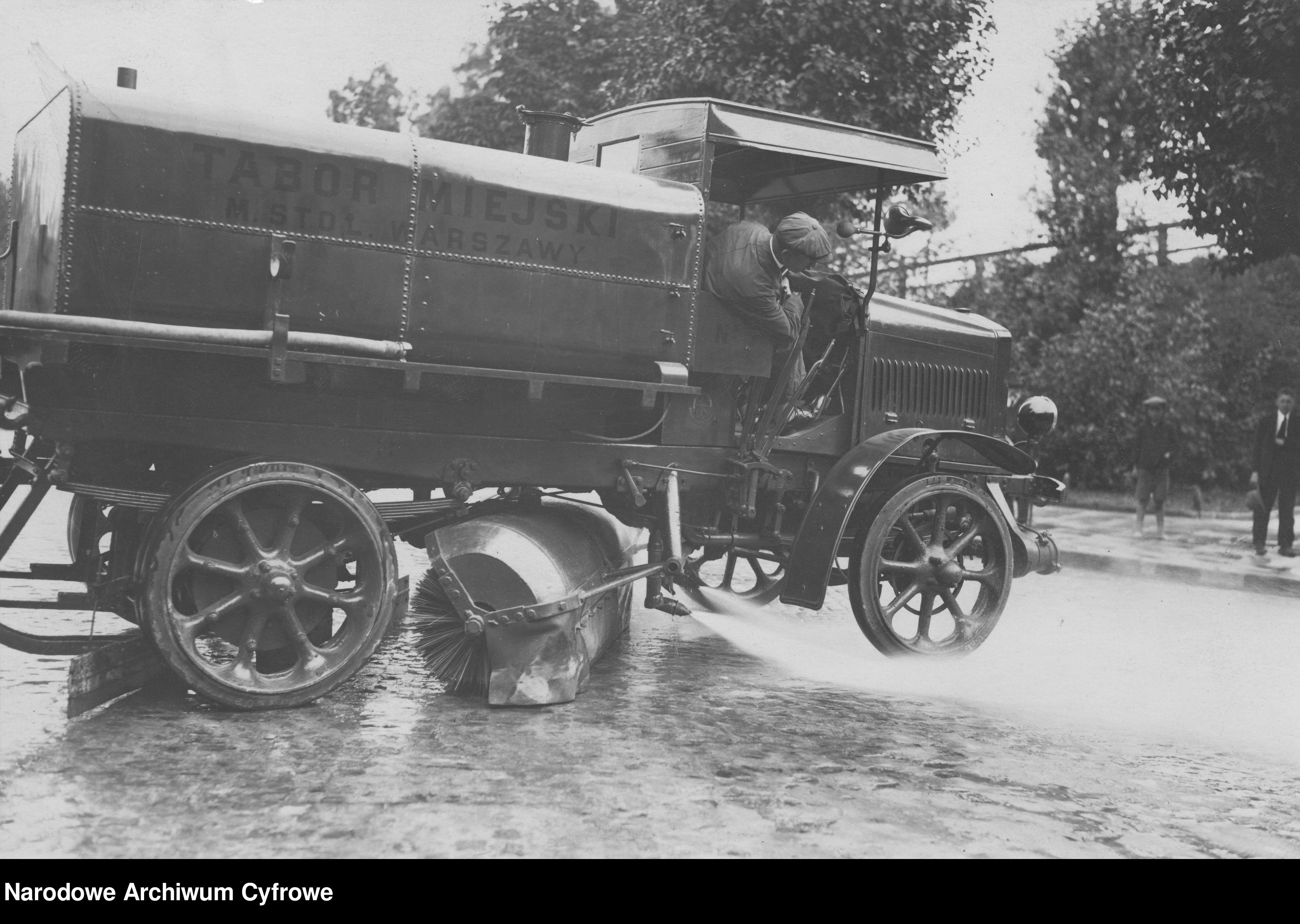 Czarno-białe zdjęcie z lat '20 XXw. historyczna zamiatarka czyści ulicę
