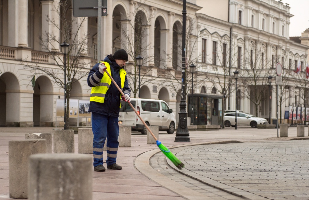 Pracownik ZOM w struju roboczym zamiata miotłą chodnik