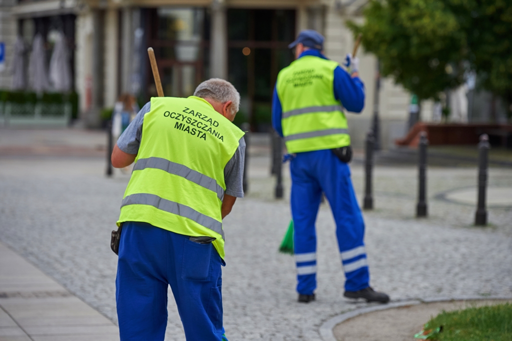 Pracownicy ekipy porządkowej Zarządu Oczyszczania Miasta zamiatają chodnik