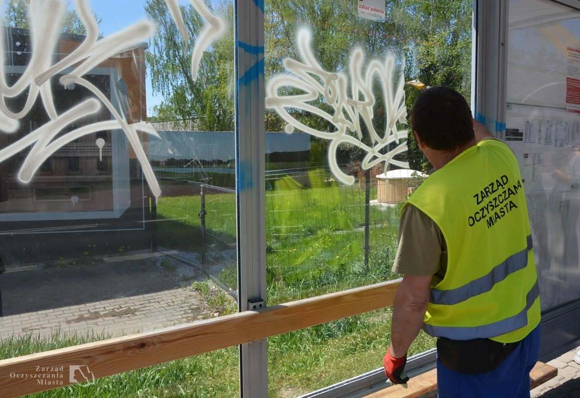 Pracownik grupy interwencyjnego sprzątania czyści wiatę z pseudograffiti