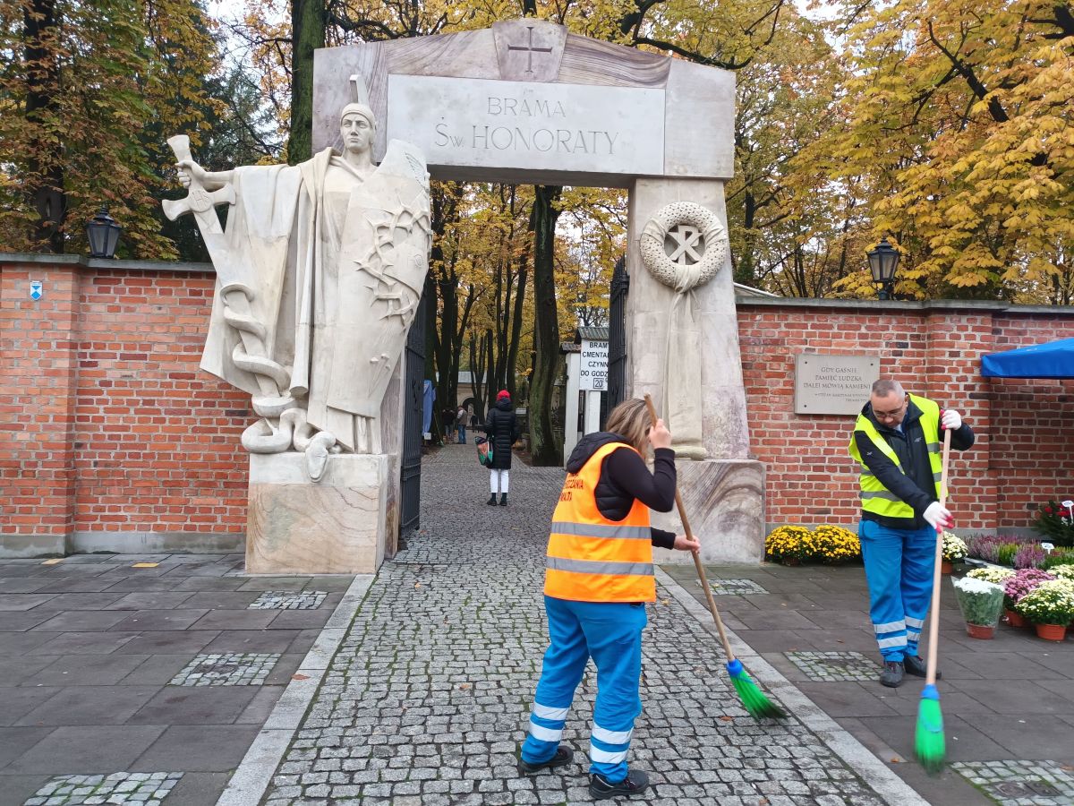 Pracownicy ZOM zamiatają chodnik przed bramą Cmentarza Powązkowskiego