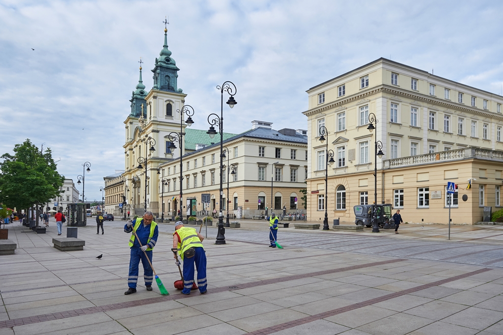 Krakowskie Przedmieście, na pierwszym planie ekipa sprzątająca zamiata chodnik, na drugim planie po drugiej stronie ulicy chodnik czyści szorowarka