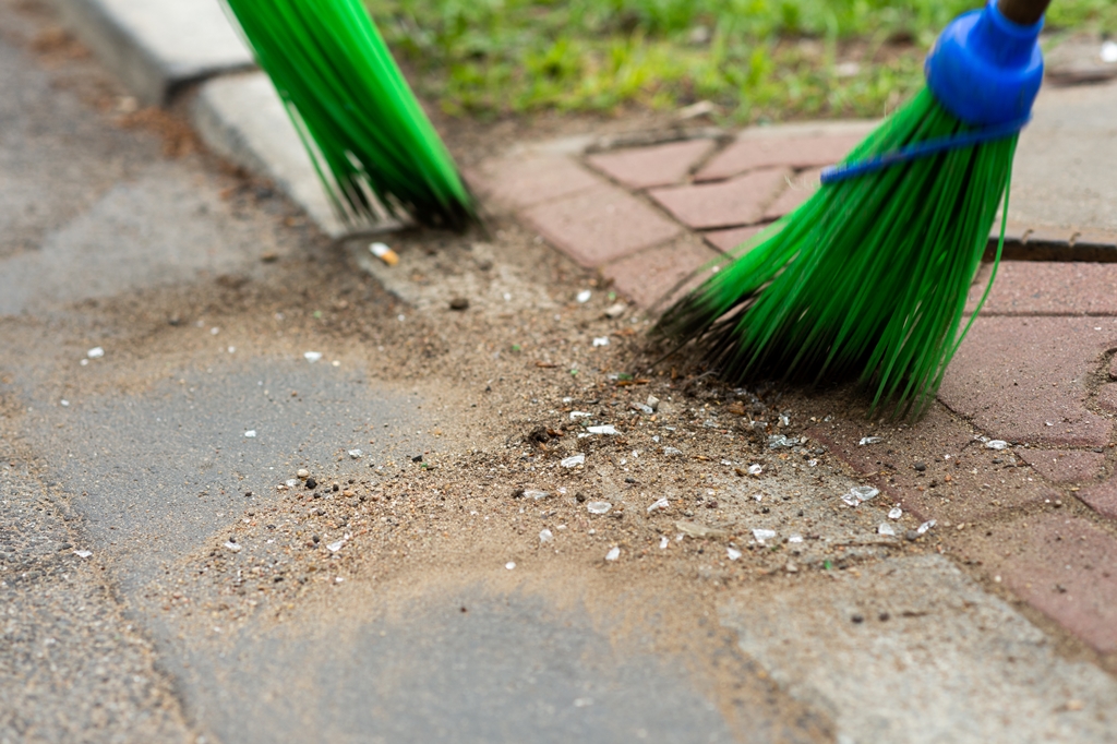 Zbliżenie na koniec miotły, która zamiata piasek i szkło ze ścieżki rowerowej
