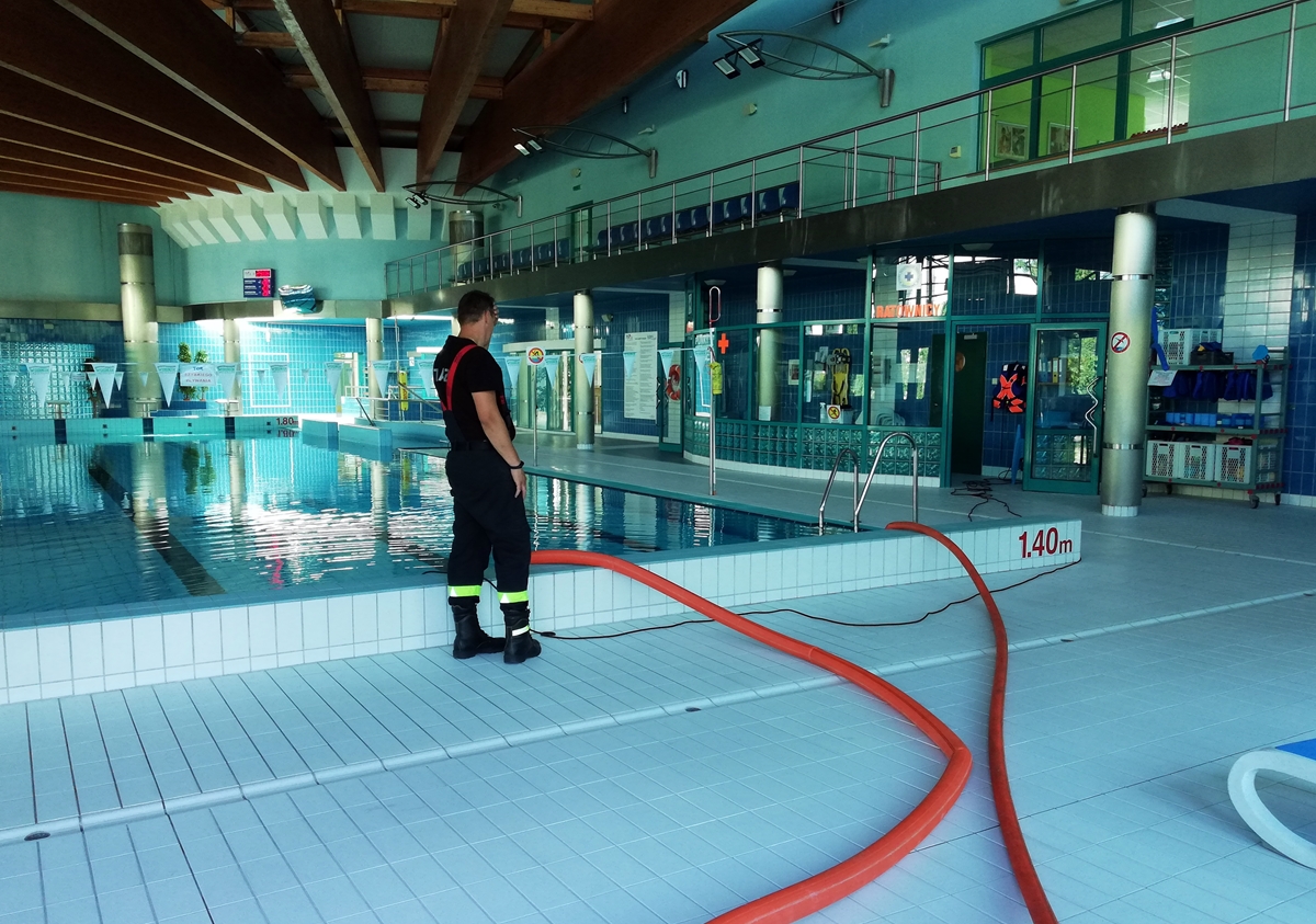 Wnętrze pływalni, strażak na brzegu basenu nadzoruje wypompowywanie wody