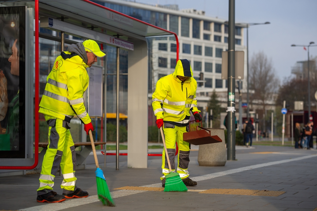 Pracownicy firmy porządkowej zamiatają chodnik na przystanku