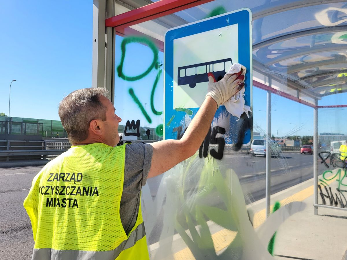 Pracownik ekipy porządkowej czyści wiatę przystankową z pseudograffiti