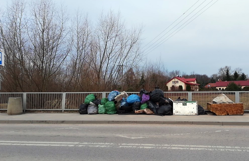 Przystanek autobusowy, na którym znajduje się bardzo dużo worków ze śmieciami i fragmentów mebli