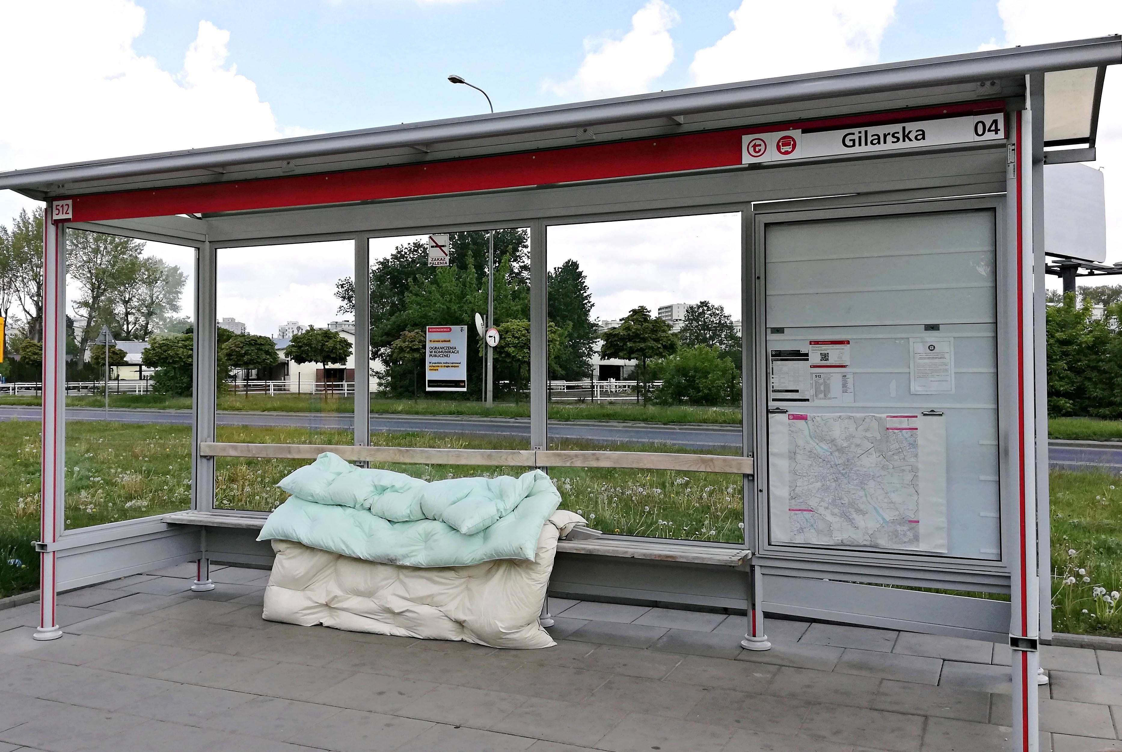 Przystanek autobusowy, na ławce pod wiatą leży kilka kołder