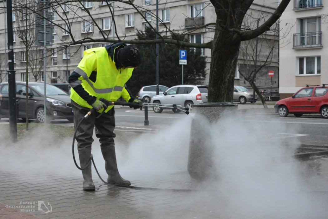 Pracownik firmy porządkowej myje betonowy kosz myjką ciśnieniową