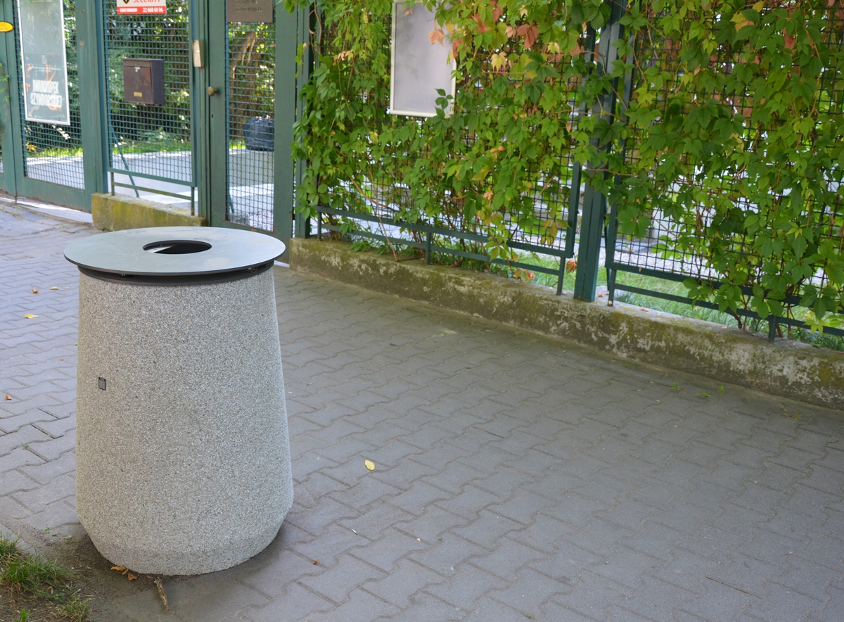 Okrągły betonowy kosz na śmieci z żeliwną pokrywą stoi na chodniku