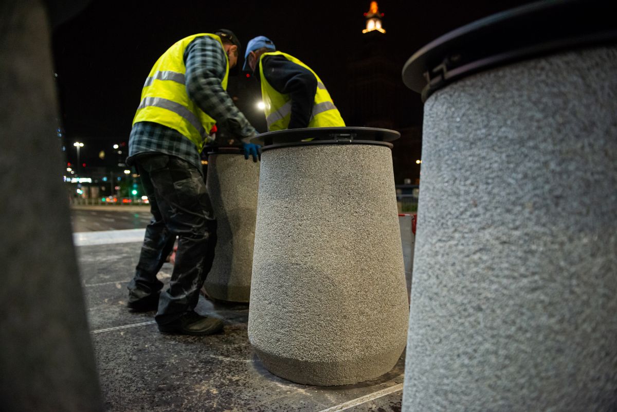 Pracownicy w odblaskowych kamizelkach przestawiają nowe betonowe kosze