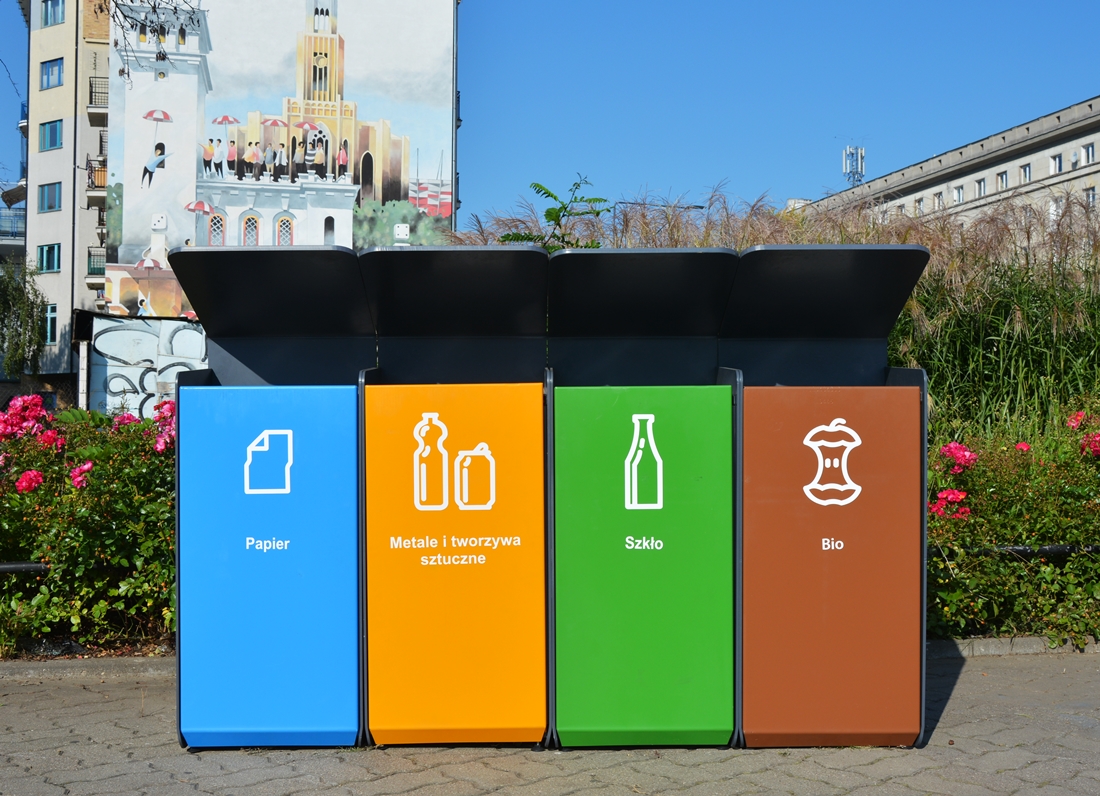Pojemnik do segregacji śmieci stojący na chodniku przy rondzie Wiatraczna. Cztery zestawione pojemniki - niebieski na papier, żółty na metale i tworzywa sztuczne, zielony na szkło i brązowy na bioodpady