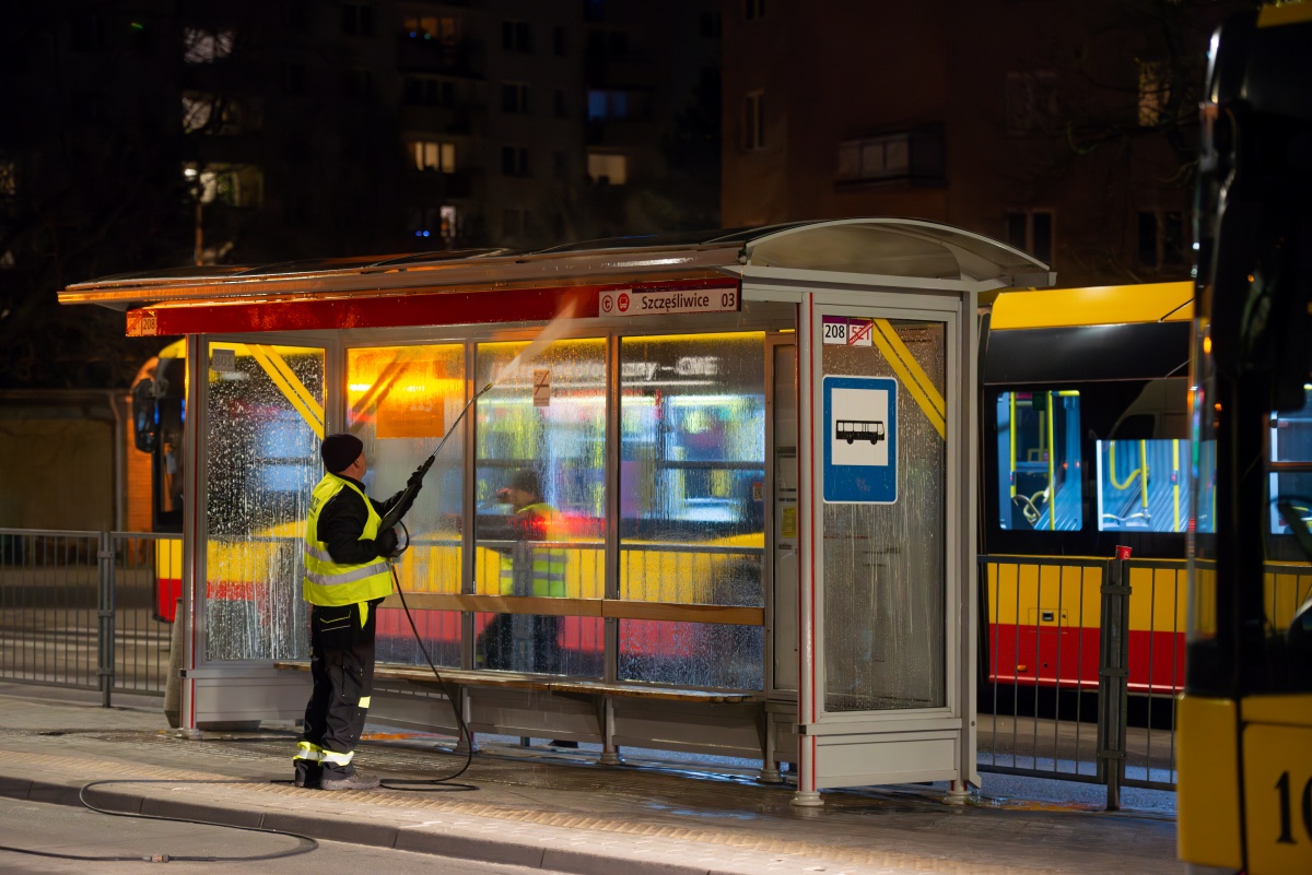 Pracownik firmy porządkowej myje wiatę przystankową myjką ciśnieniową, jest noc