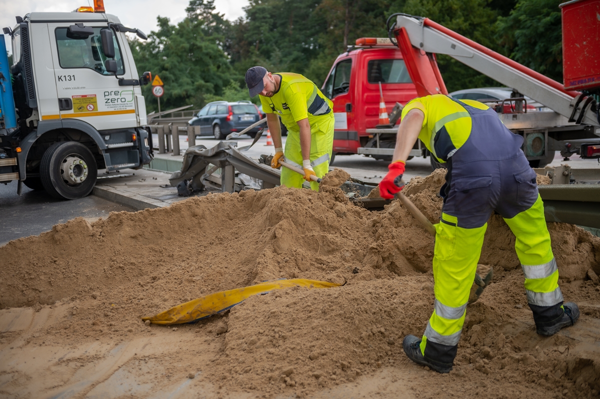 Pracownicy Pogotowia Porządkowego sprzątają łopatami duże ilości piasku z jezdni, w tle ciężarówka