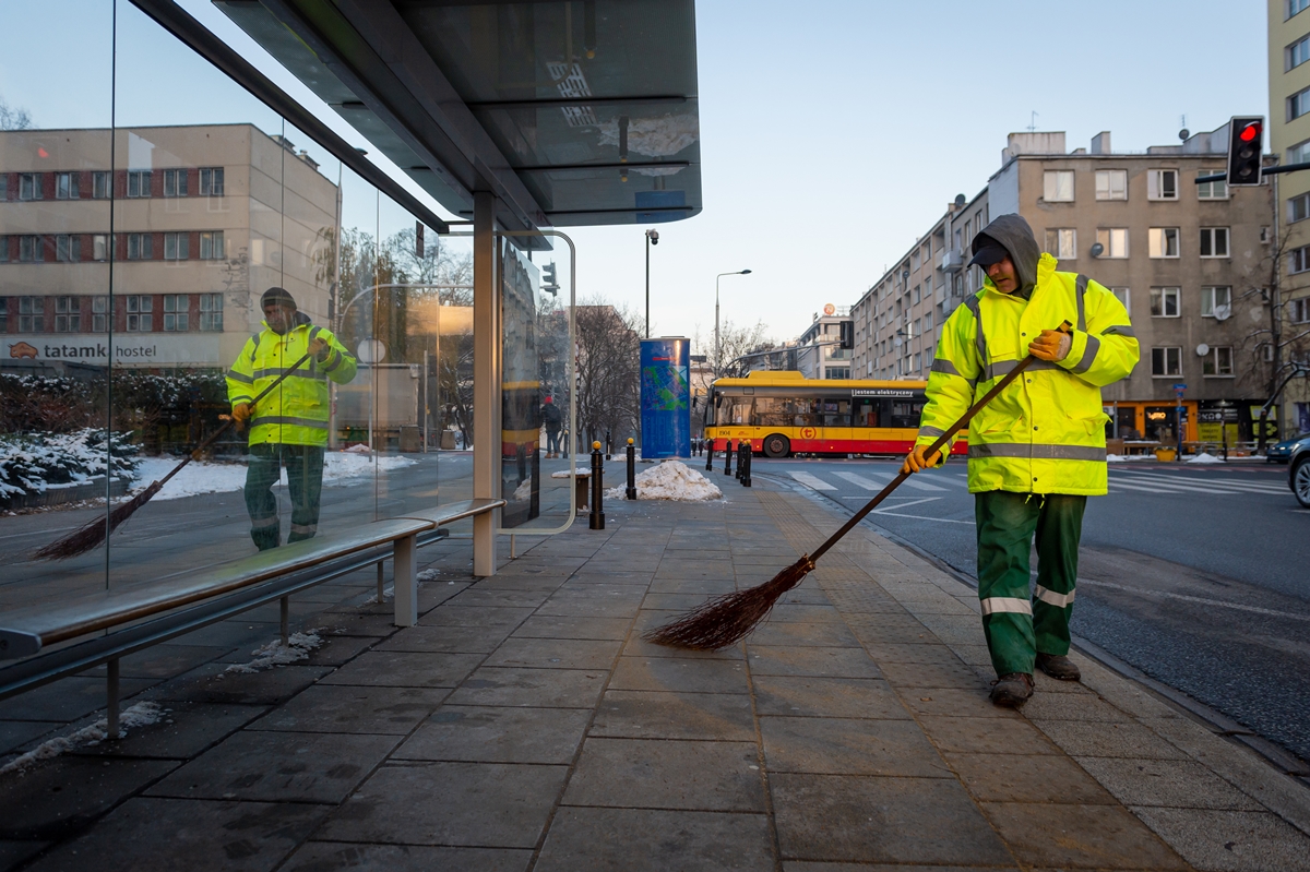 Dwóch pracowników firmy sprzątającej zamiata przystanek autobusowy
