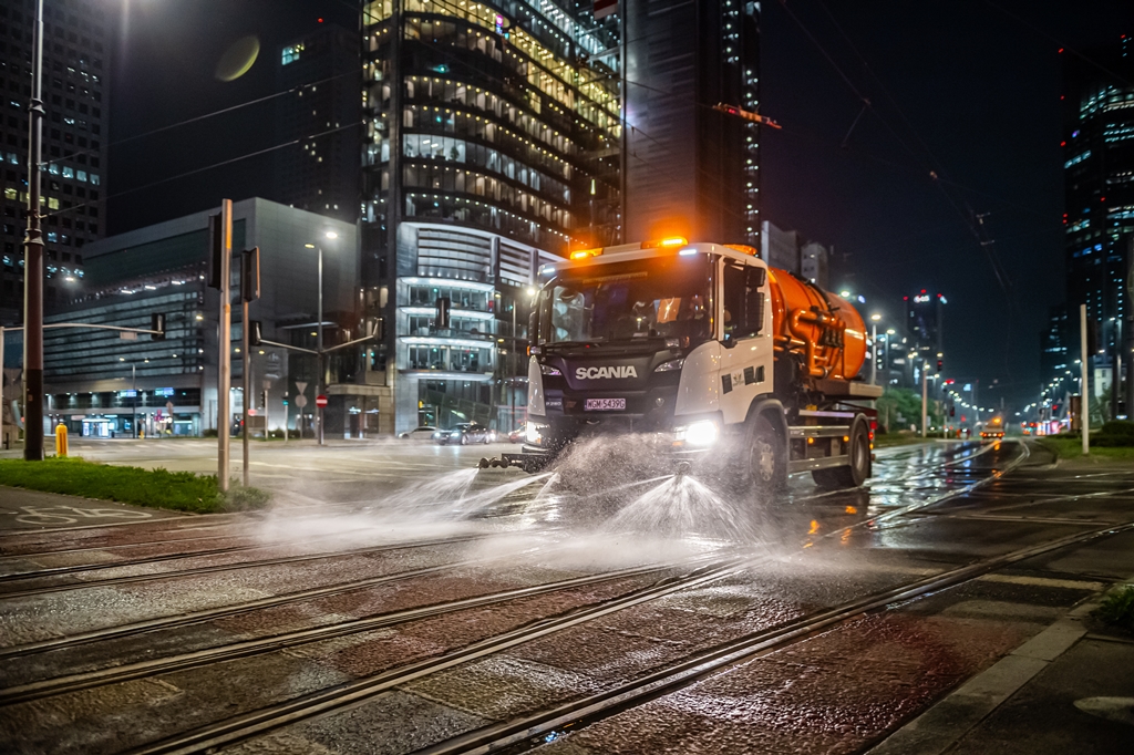 Noc, polewaczka czyści torowisko tramwajowe, w tle wieżowce