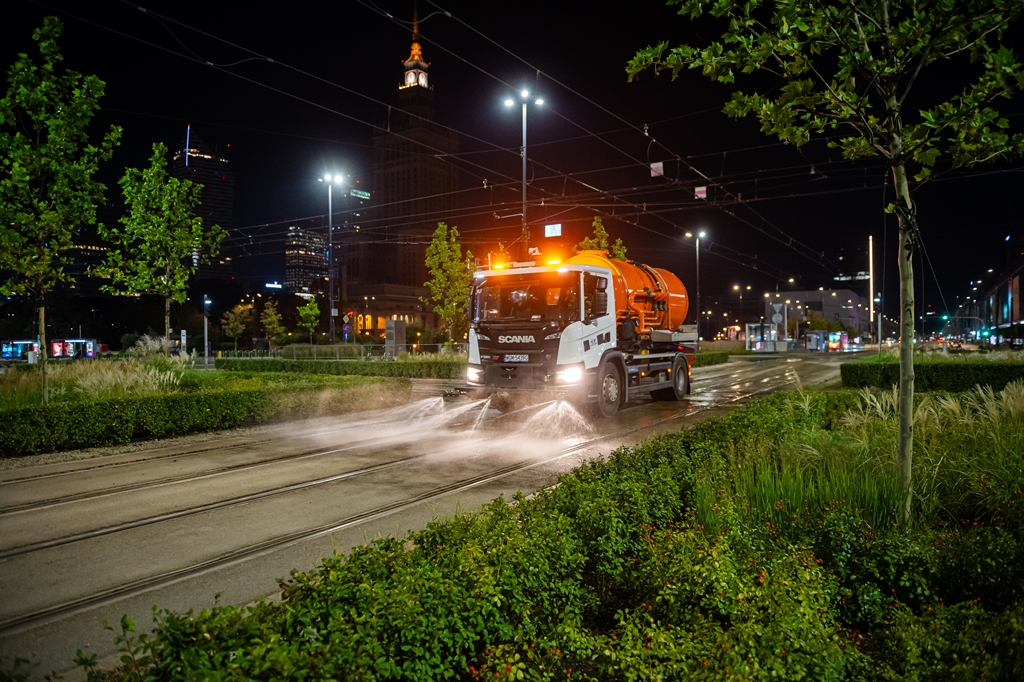 Noc, pojazd-zmywarka myje torowisko tramwajowe, na drugim planie Pałac Kultury i Nauki