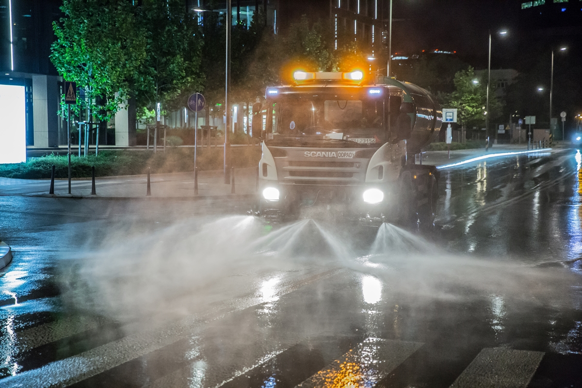Pojazd - zmywarka myje ulicę w nocy, w tle wieżowce