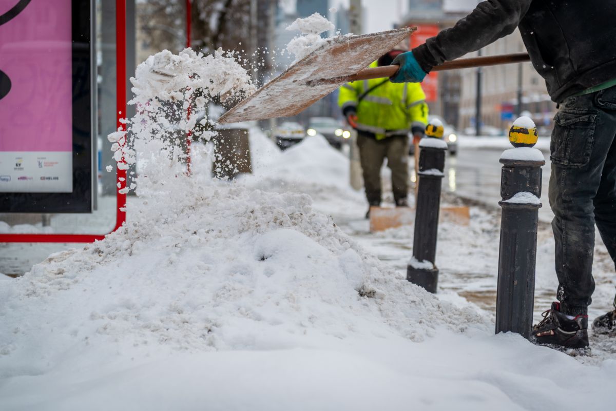 Pracownicy firmy porządkowej odśnieżają przystanek autobusowy szuflai, jest dużo śniegu