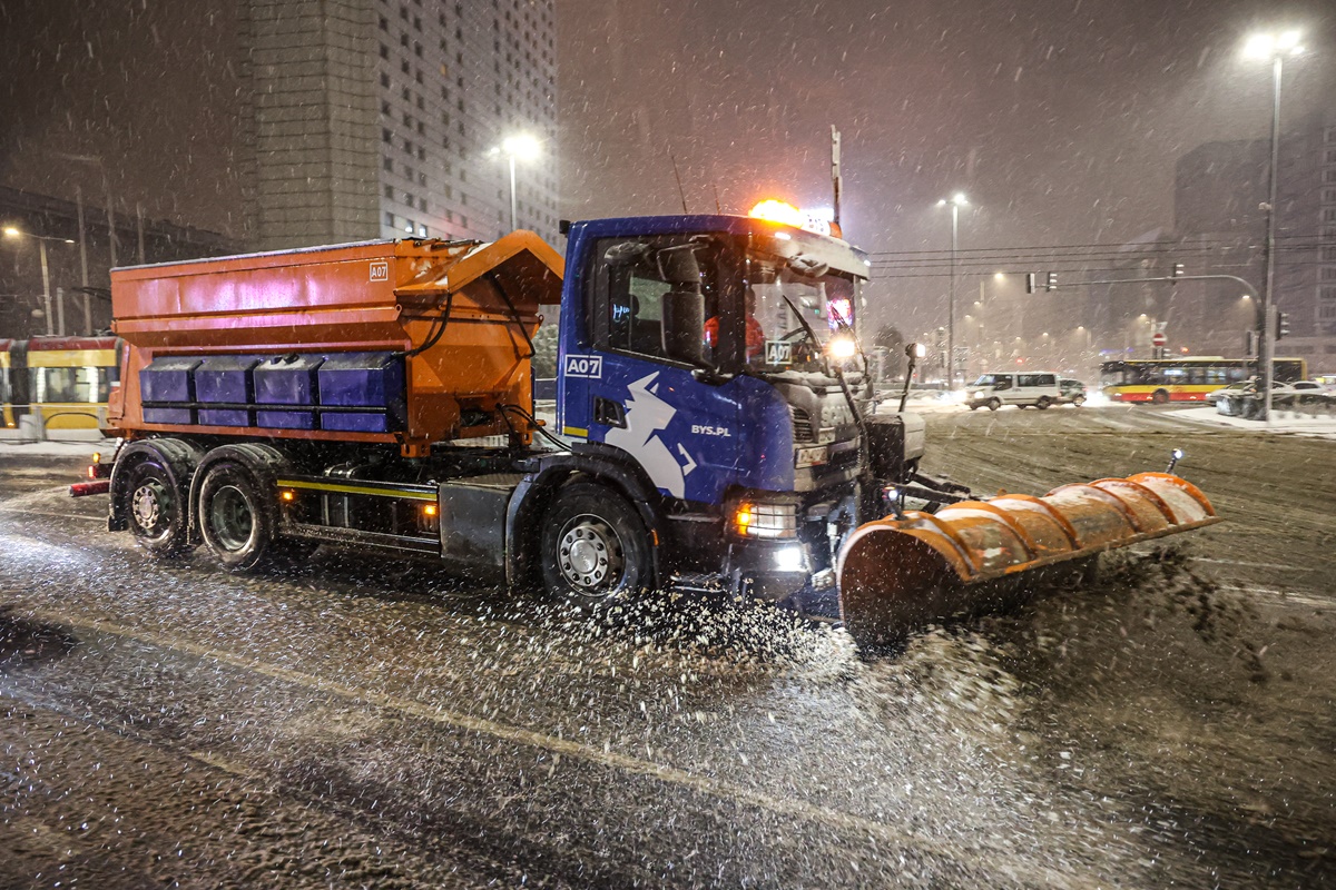 Pługoposypywarka na warszawskiej ulicy, jest noc, pada intensywny śnieg