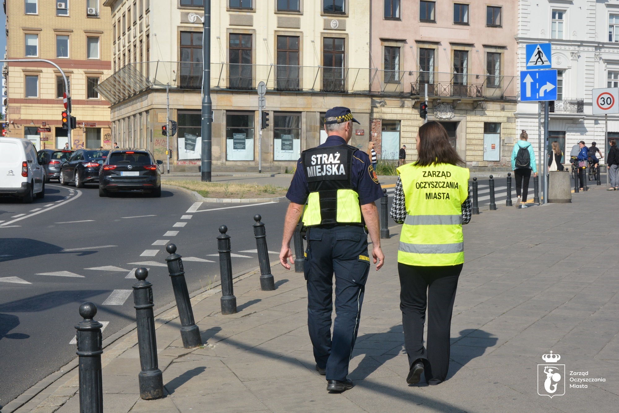 Funkcjonariusz Straży Miejskiej i kontrolerka ZOM patrolują miasto, w tle ulica i kamienica