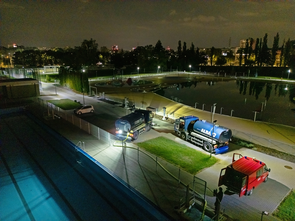 Pobieranie wody z basenów otwartych, widok na baseny z góry, w tle miasto nocą, zmywarki pobierają wodę