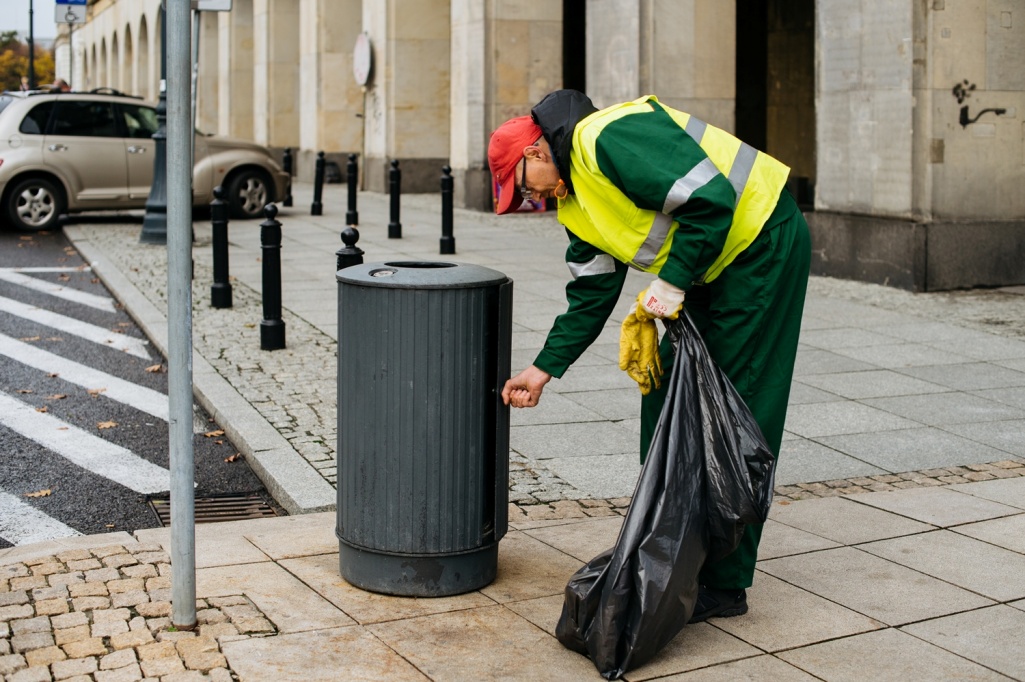 Precownik firmy porządkowej opróżnia kosz, w tle parking samochodowy