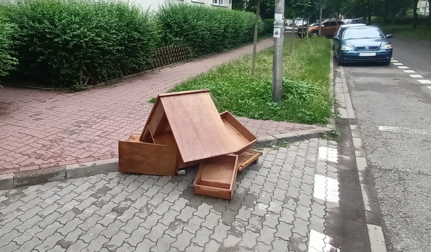 Zużyte meble leżą na chodniku, w tle trawnik, blok mieszkalny, zaparkowane samochody