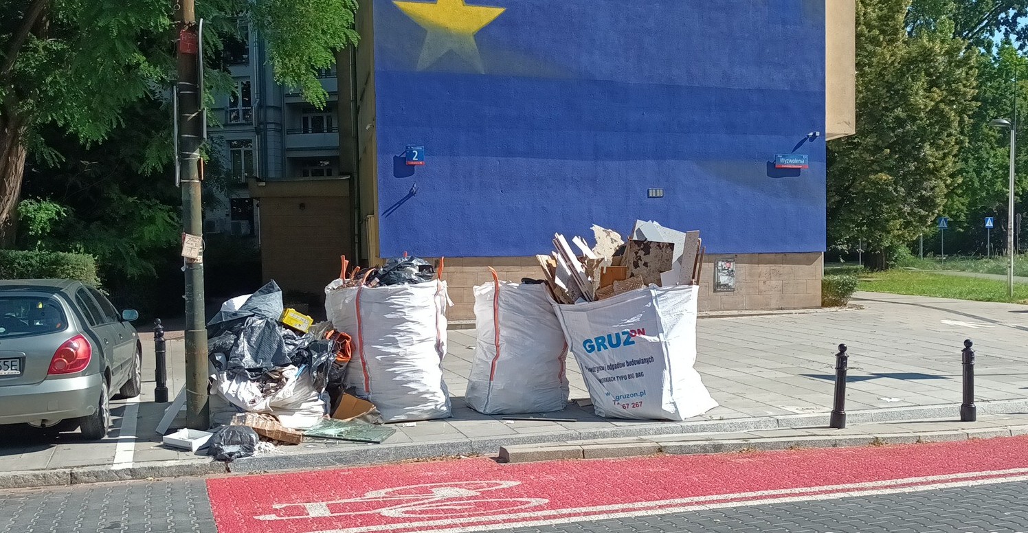 Worki typu big bag leżą pozostawione na chodniku, w tle blok mieszkalny