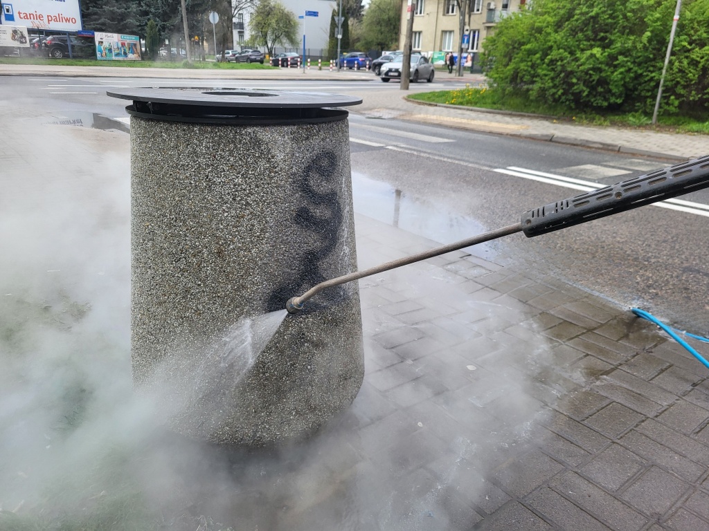 Zbliżenie na kosz, z którego usuwane jest pseudograffiti za pomocą wody pod ciśnieniem