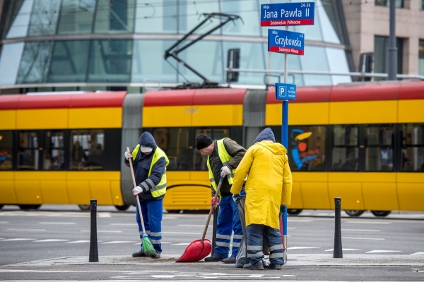 Pracownicy grupy interwencyjnego sprzątania ZOM zamiatają chodnik, w tle jedzie tramwaj