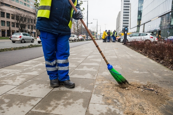 Pracownik grupy interwencyjnego sprzątania ZOM zamiata piasek z chodnika