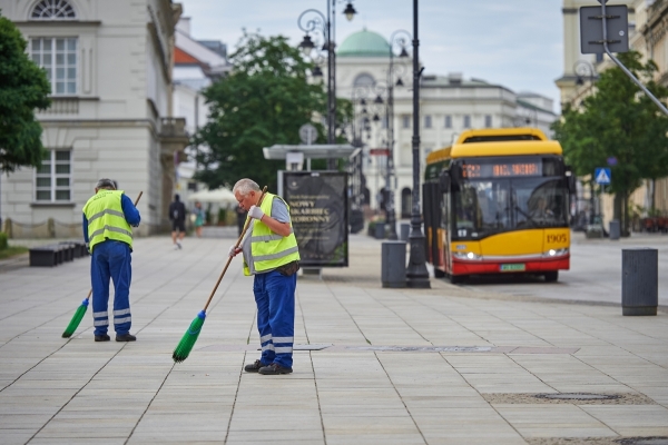 Pracownicy grupy interwencyjnego sprzątania ZOM zamiatają chodnik, w tle autobus na przystanku