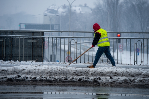 Pracownik zgarnia szuflą śnieg z chodnika na moście