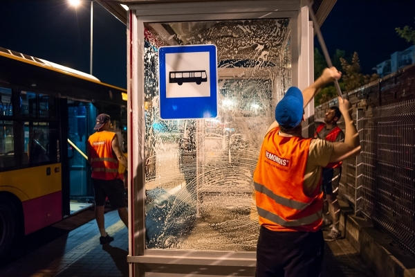 Pracownicy firmy porządkowej myją nocą wiatę przystankową